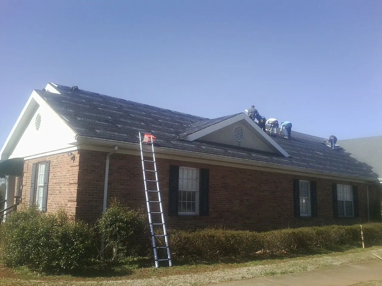 Crew tearing shingles off a brick ranch roof with a ladder set — Metal Roof Repair work by our crew in Glenville