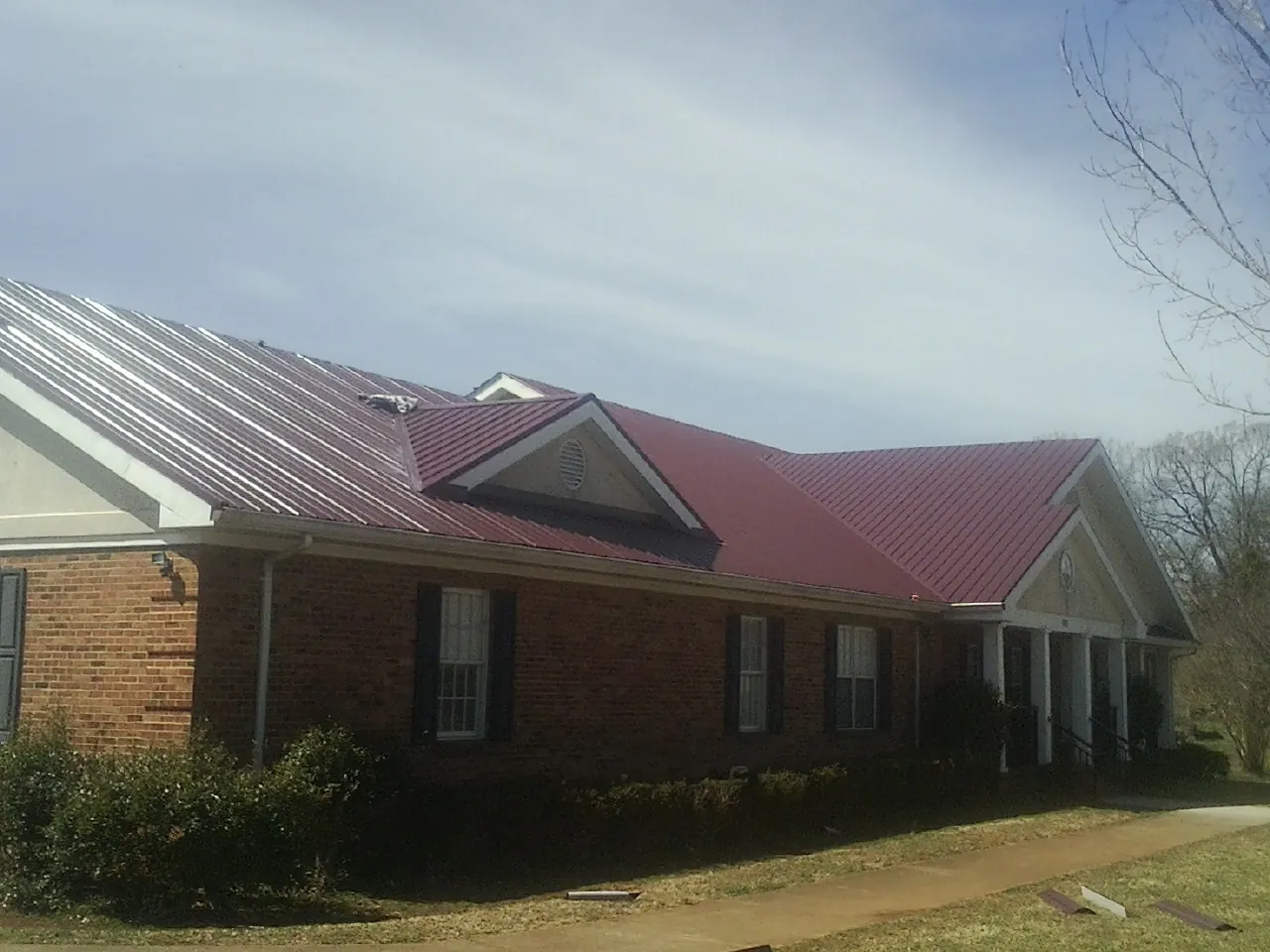 Red metal roof with gabled entries on a long brick building, from a Hail Damage Roof Repair job in Glenville
