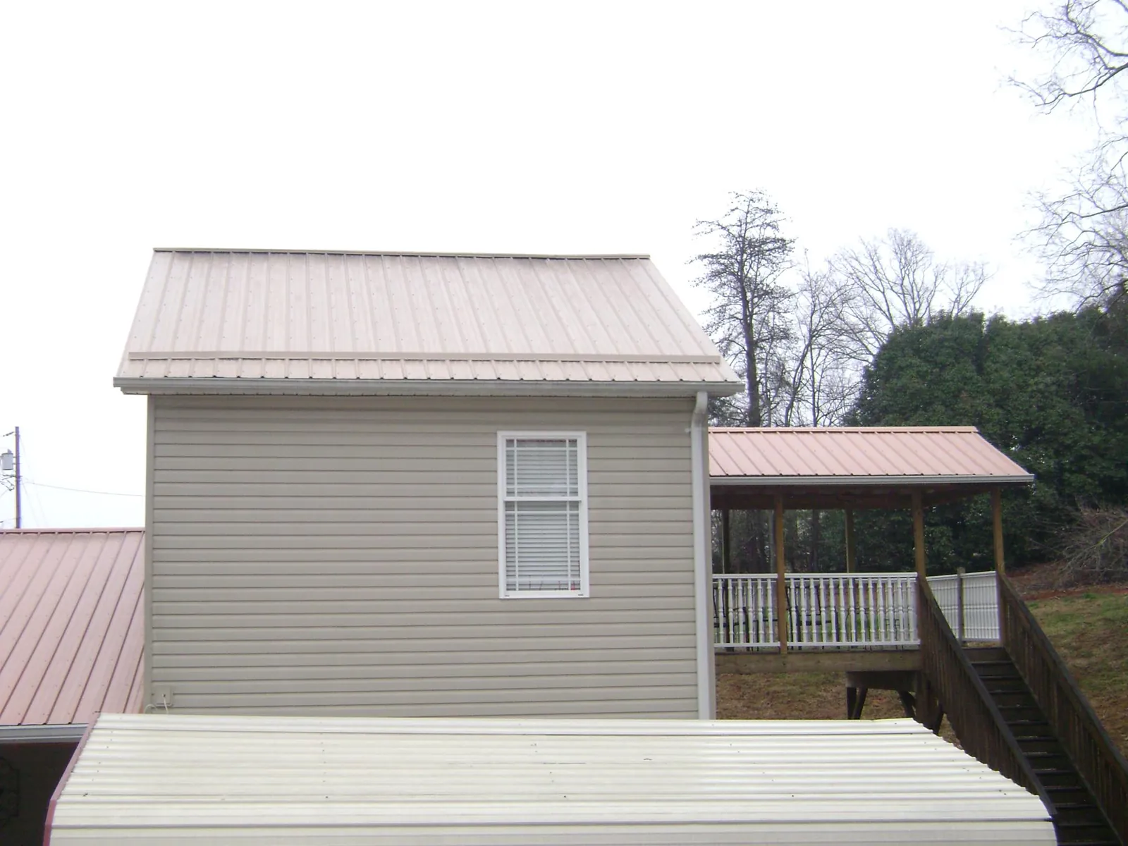 Tan metal roofs on a two story addition and attached porch, from a Roof Replacement job in Glenville